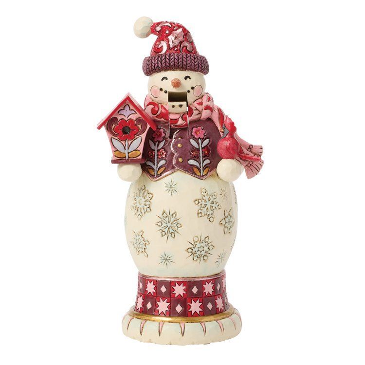 Een sneeuwpopfiguur in kleding met een patroon, die een vogelhuisje vasthoudt.