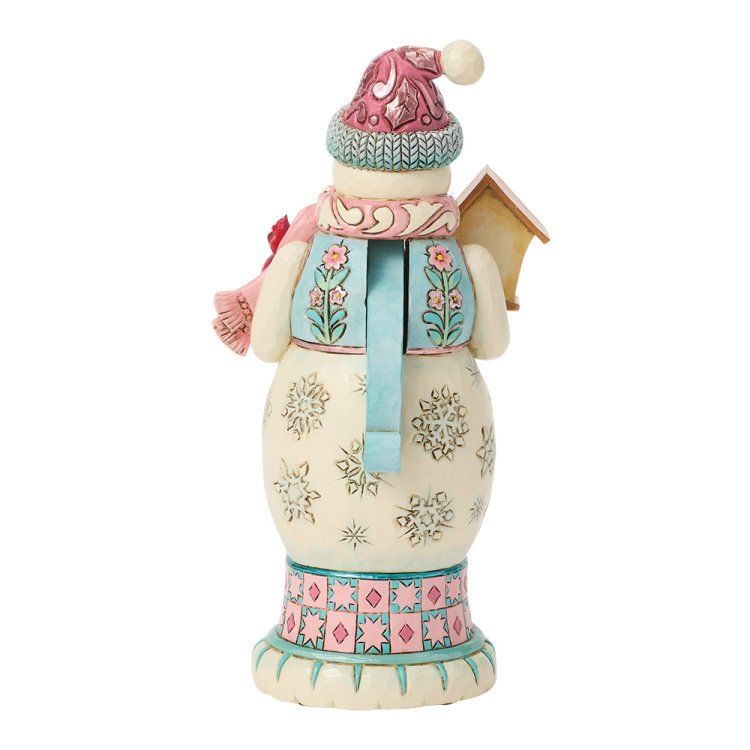 Een sneeuwpopfiguurtje met een roze muts, sjaal en vest, en een vogelhuisje op zijn rug.