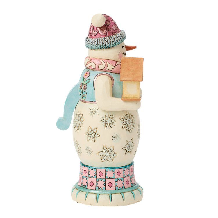 Een sneeuwpopfiguurtje dat een lampje vasthoudt, een roze hoed draagt, een blauw vest aanheeft en een lijfje met een patroon heeft.