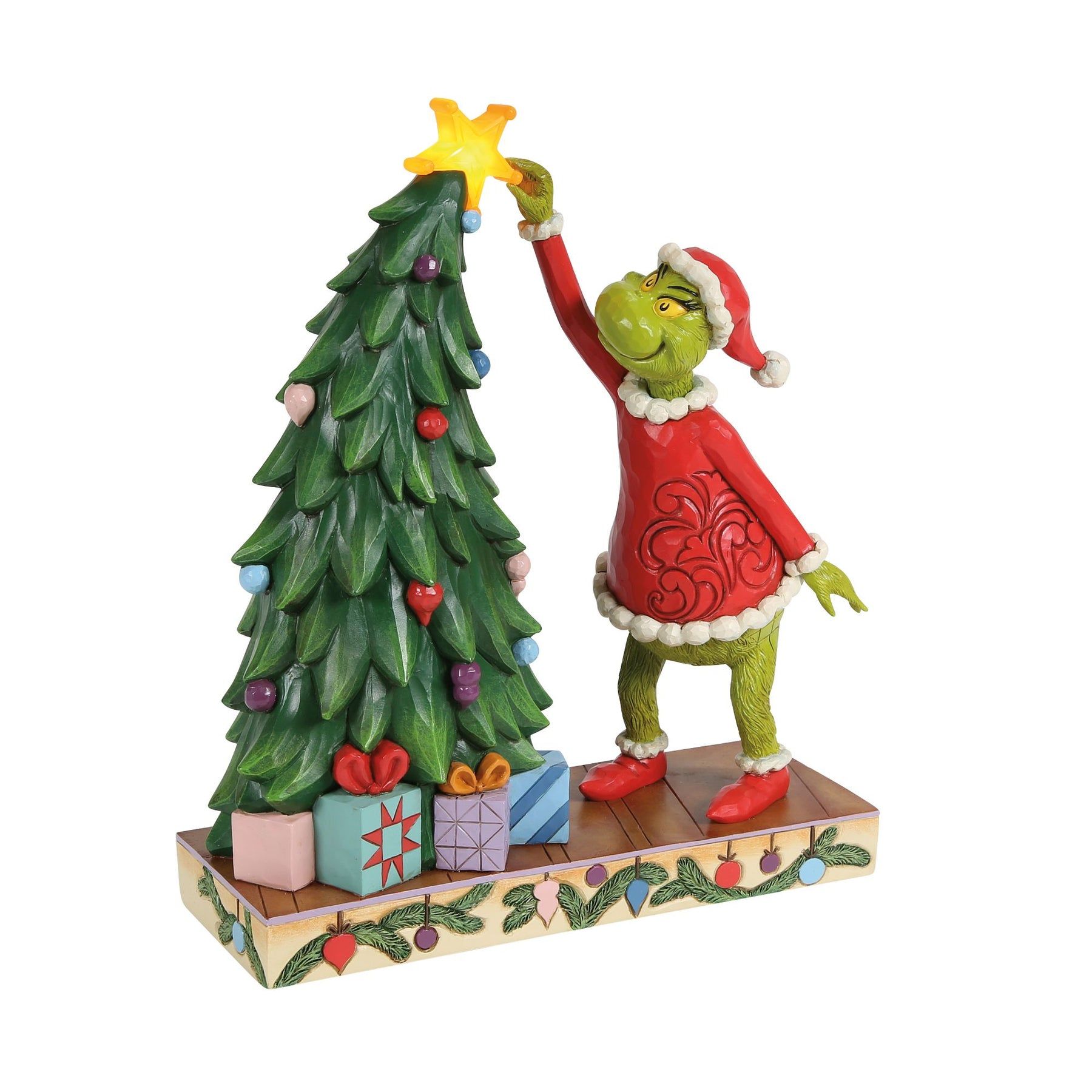 De Grinch plaatst een ster in de kerstboom. De Grinch draagt een rood pak en een kerstmuts.