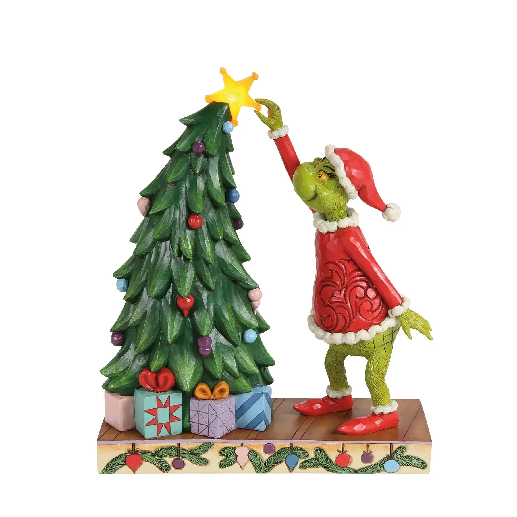 De Grinch plaatst een ster bovenop een kerstboom, versierd met cadeautjes op een voetstuk met lichtjes.