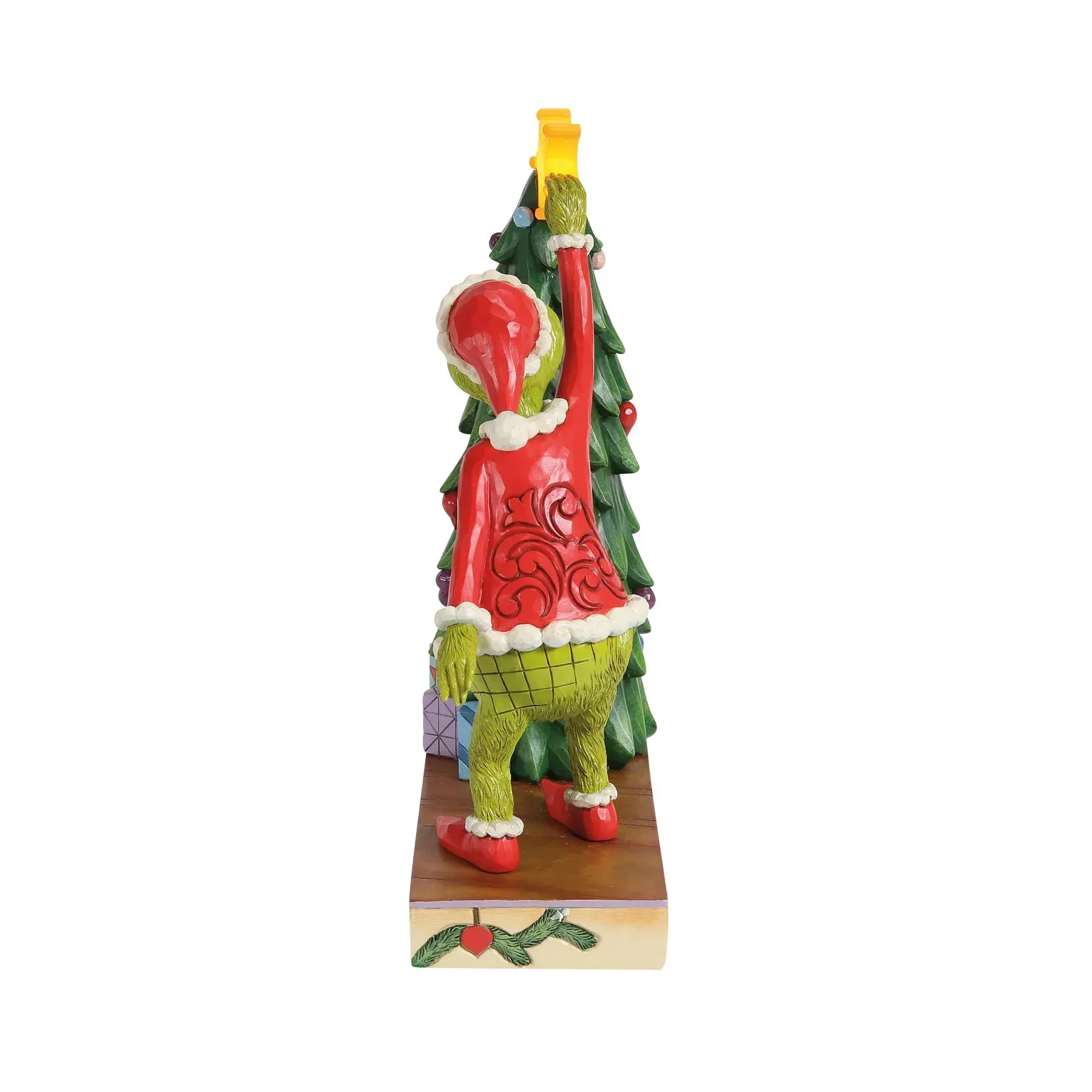 De Grinch plaatst een ster bovenop een kerstboom, versierd met cadeautjes op een voetstuk met lichtjes.