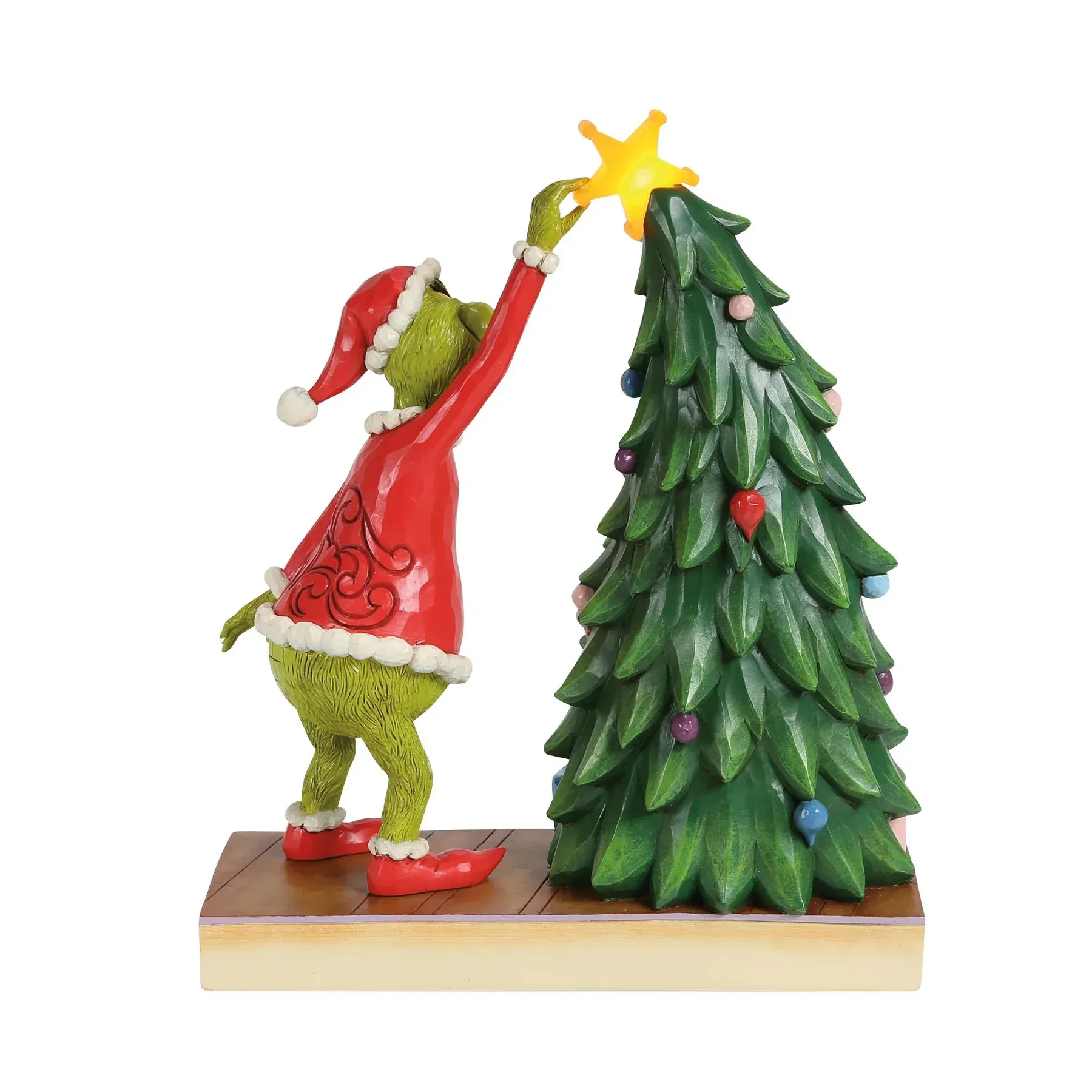 De Grinch in een kerstmanpak plaatst een ster in een versierde kerstboom.