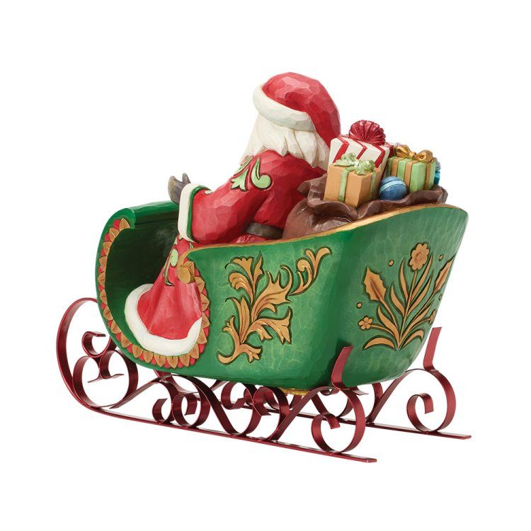 De Kerstman zit in een groene slee en houdt een zak met cadeaus vast. De slee heeft bordeauxrode metalen glijders.