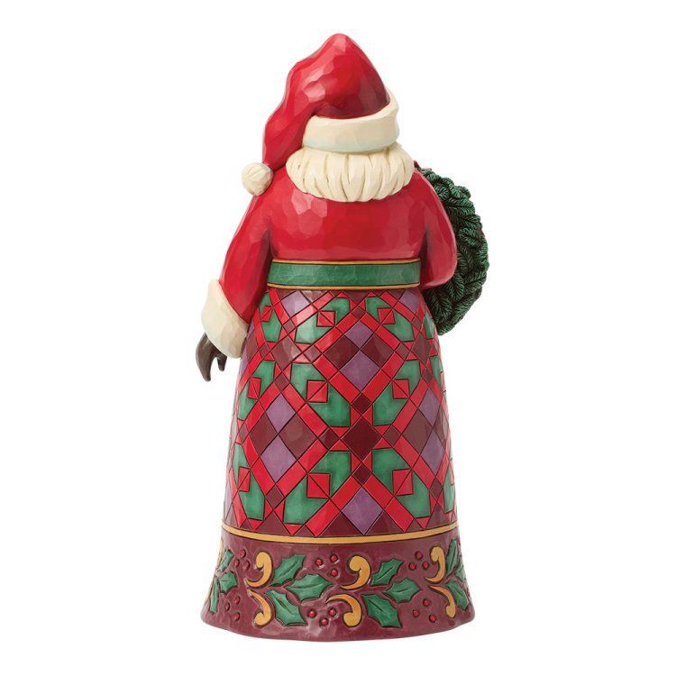 Een kerstmanfiguur in een rode jas met een rok met patroon, die een kerstkrans vasthoudt.