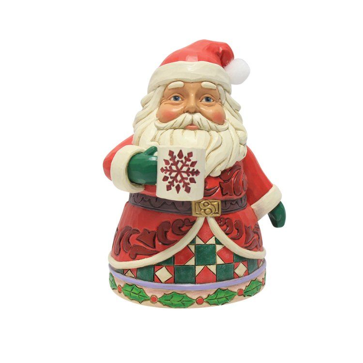 Een kerstmanfiguurtje met een mok met sneeuwvlokkenmotief. Hij draagt ​​een rode jas en een rode muts.