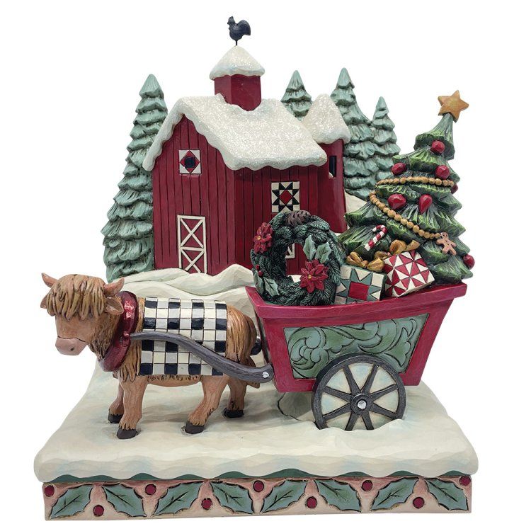 Een koe trekt een kar met een kerstboom en cadeaus voor een rode schuur in een besneeuwd landschap.