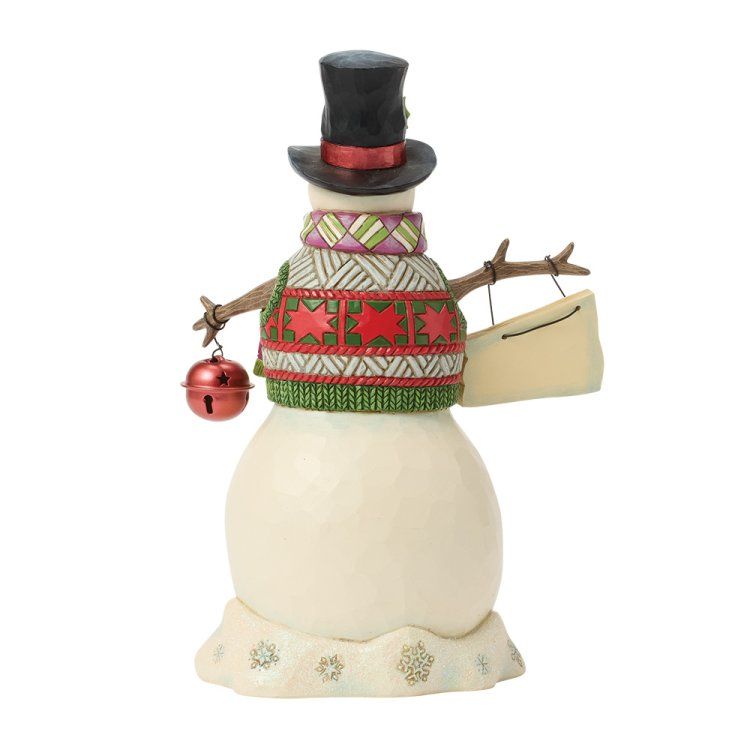 Een sneeuwpopfiguur met een hoed en sjaal, die een bel en een bordje vasthoudt.