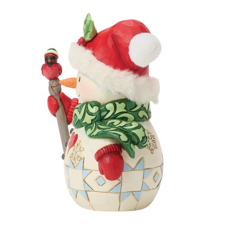 Een sneeuwpopfiguur met rode muts en groene sjaal, die een staf met een vogel vasthoudt.