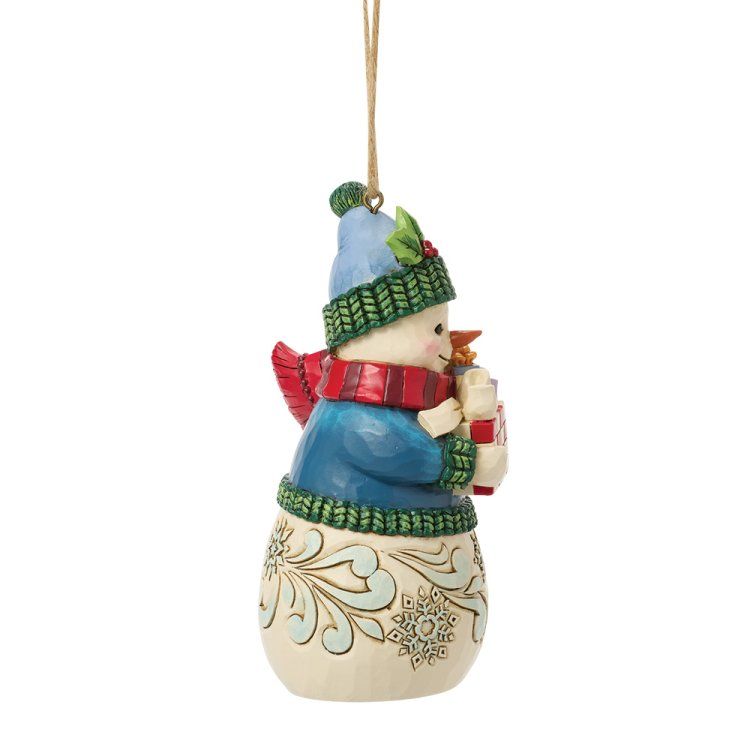 Een sneeuwpop als kerstversiering met een blauwe muts, sjaal en jas, die een cadeautje vasthoudt.