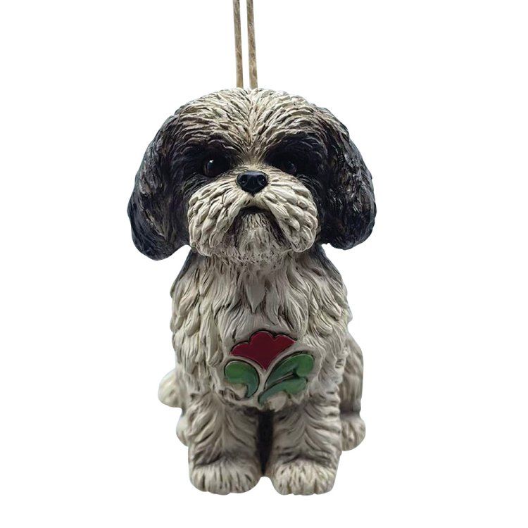 Een ornament in de vorm van een Shih Tzu-hond, met zwart-witte vacht, die een rood-groene bloem vasthoudt, hangend aan een touwtje.