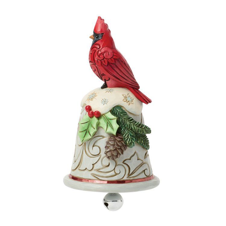 Een rode kardinaal zit bovenop een feestelijk belvormig ornament met hulst, dennenappels en sierlijke krullen.