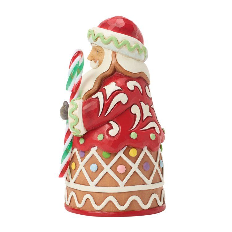 Een kerstmanfiguur met een voetstuk van peperkoek, een rode jas en een zuurstok in zijn hand.