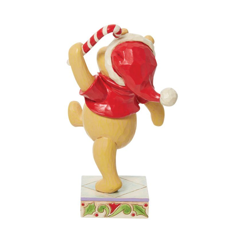 Een Winnie de Pooh-figuurtje met een kerstmuts op en een zuurstok in zijn hand, op een versierde sokkel.