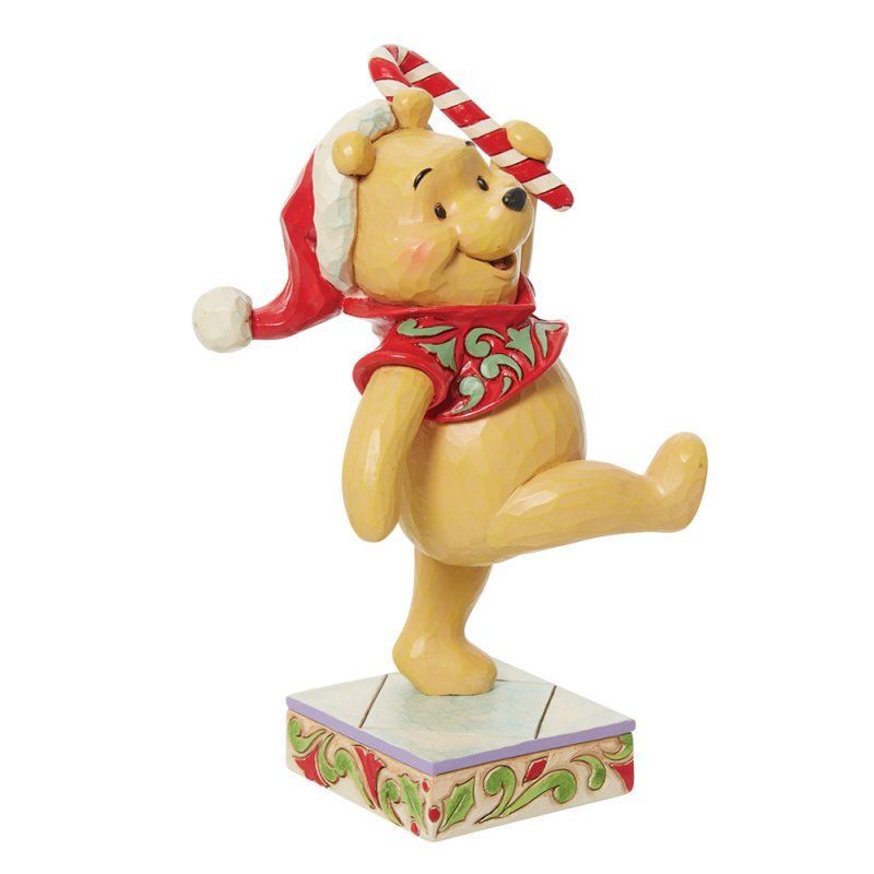 Een Winnie de Pooh-figuurtje met een kerstmuts op, die een zuurstok vasthoudt en op een doos danst.