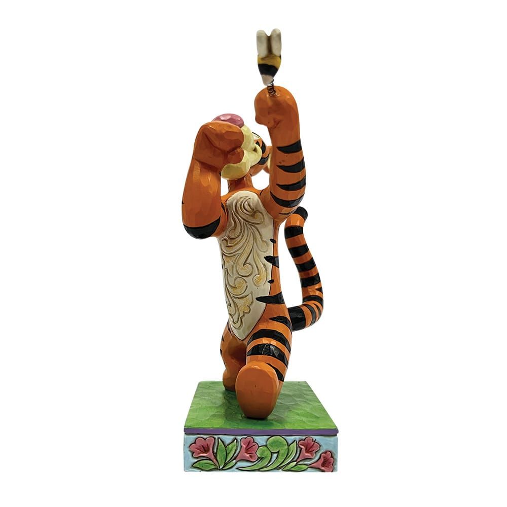 Tigger-figuurtje dat naar een bij reikt. Oranje en zwarte strepen, lachend, op een versierde sokkel.