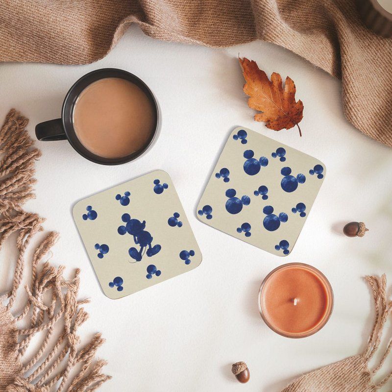 Twee Mickey Mouse-onderzetters met een koffiekopje, een kaars en herfstdecoratie.