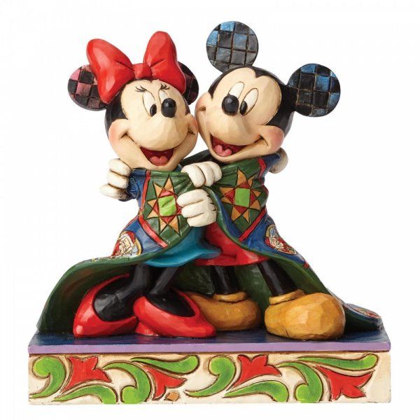 Mickey en Minnie Mouse omhelzen elkaar, gekleed in versierde outfits, en staan op een sokkel met een patroon.