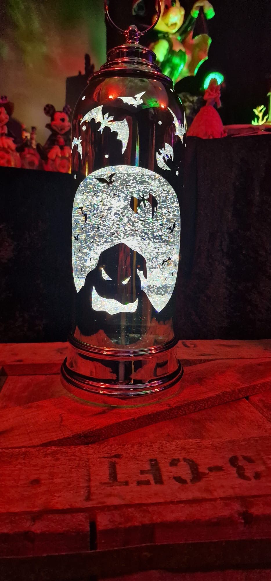 Een glanzende, metalen lantaarn met een uitgesneden patroon. Hij staat op een rode, houten ondergrond, met andere decoraties op de achtergrond.