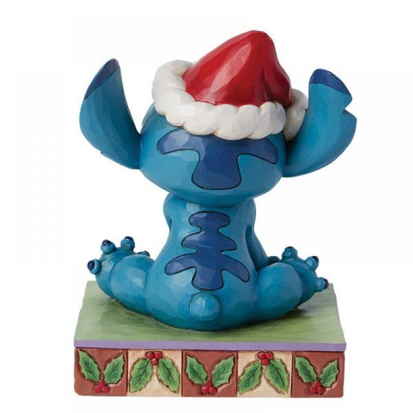 Een figuurtje van Blue Stitch met een kerstmuts op, zittend op een versierde sokkel.