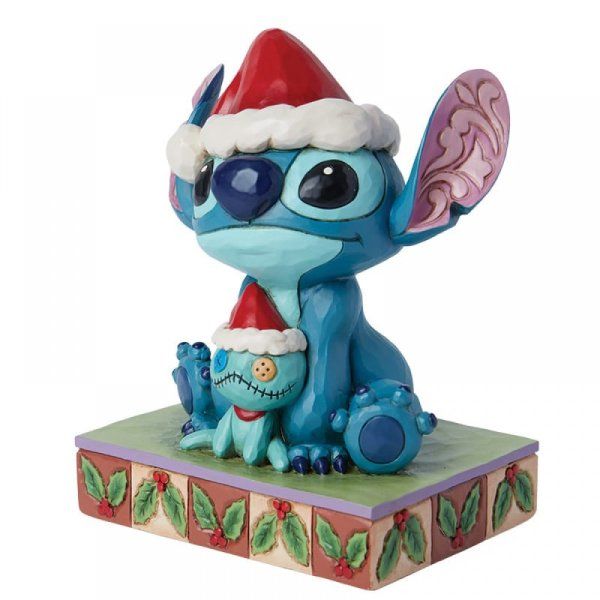 Een Stitch-figuurtje met een kerstmuts op, dat een kleiner Stitch-speeltje met een kerstmuts vasthoudt, op een versierde sokkel.