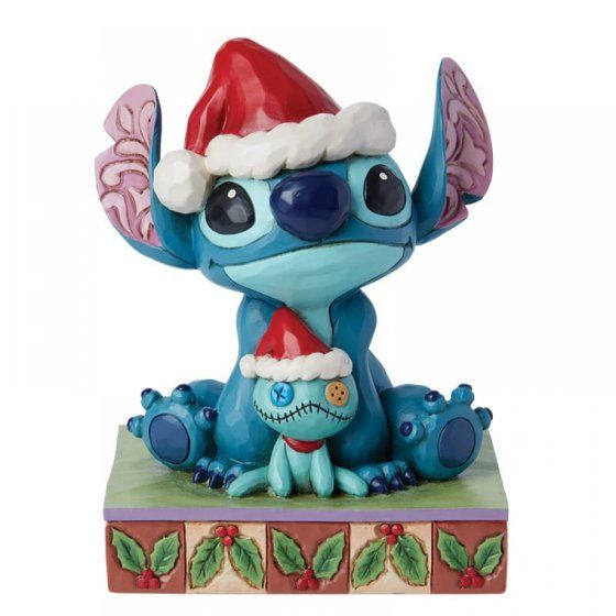 Een Stitch-figuurtje met een kerstmuts op, dat een kleiner Stitch-speeltje met een kerstmuts vasthoudt, op een versierde sokkel.