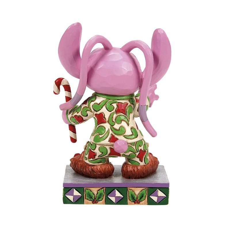 Een engeltje in kerstpyjama met een zuurstok in zijn hand, staand op een versierde sokkel.