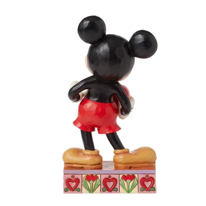 Een Mickey Mouse-figuurtje dat een rood hartje vasthoudt, staat met een glimlach op een versierde sokkel.