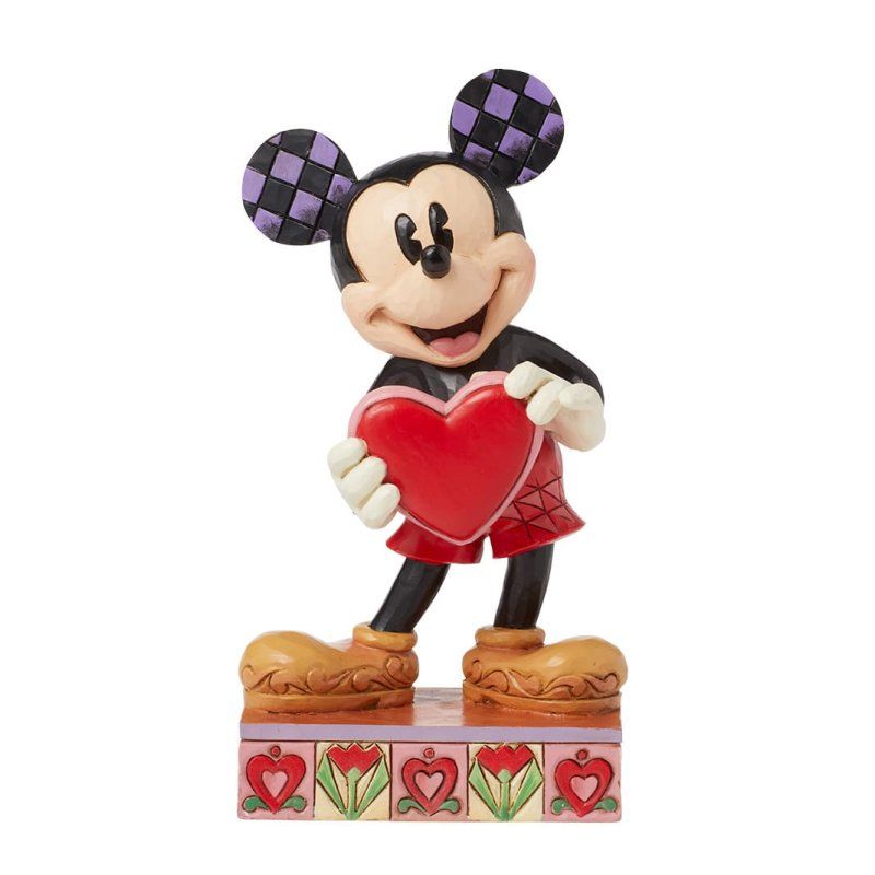 Een Mickey Mouse-figuurtje dat een rood hartje vasthoudt, staat met een glimlach op een versierde sokkel.