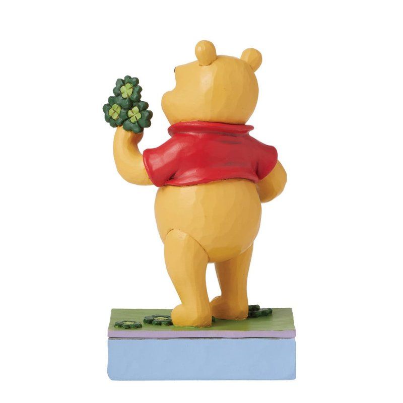 Winnie de Poeh houdt een pot met goud en klavertjes vier vast, op een voetstuk met een regenboog.
