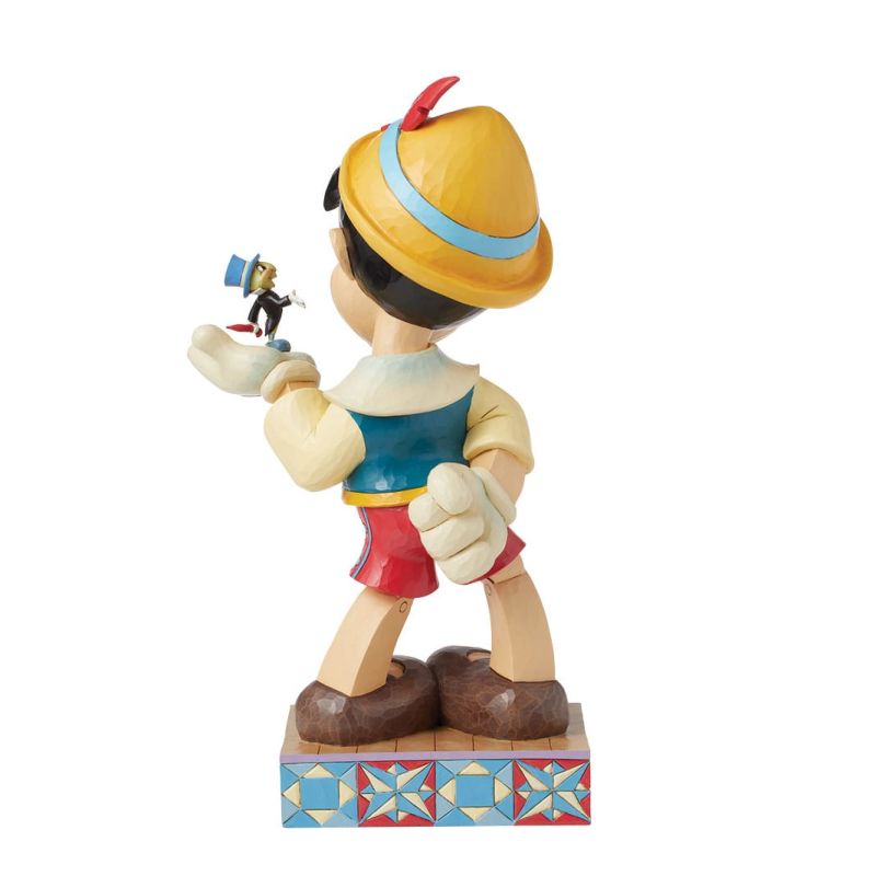 Een Pinocchio-beeldje dat Japie Krekel vasthoudt, lachend, op een versierde sokkel.