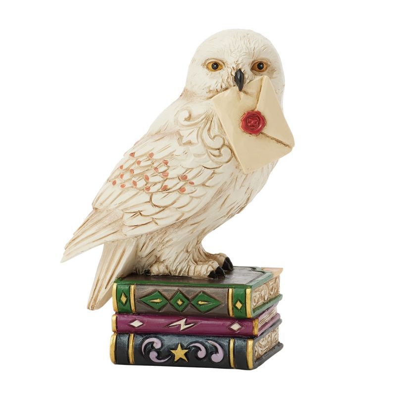 Een witte uil met een brief zit op een stapel kleurrijke boeken.