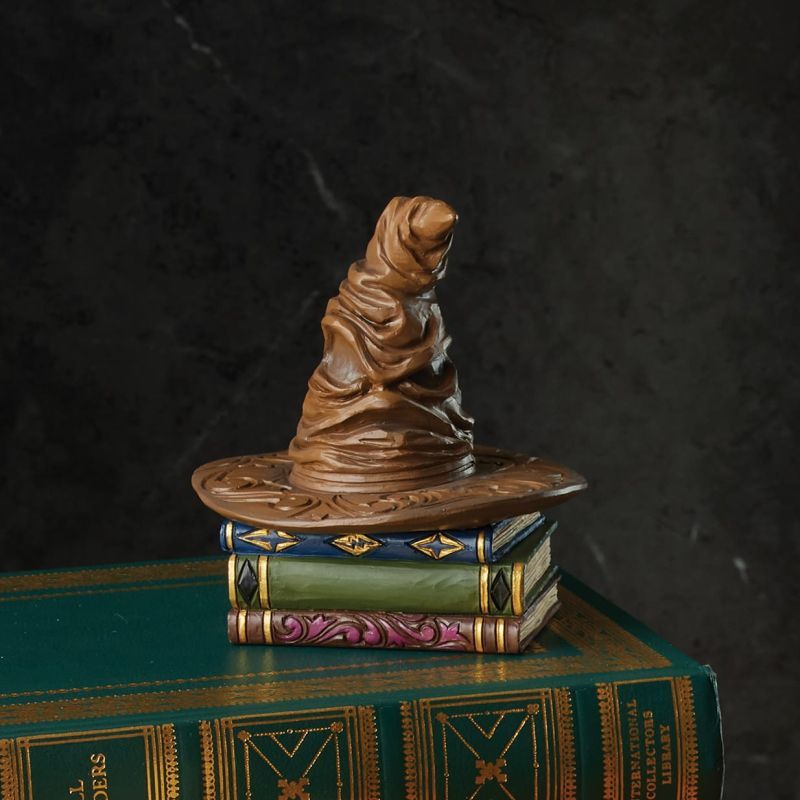 Een beeldje van de Sorteerhoed op een stapel boeken, in bruin-gouden kleuren.