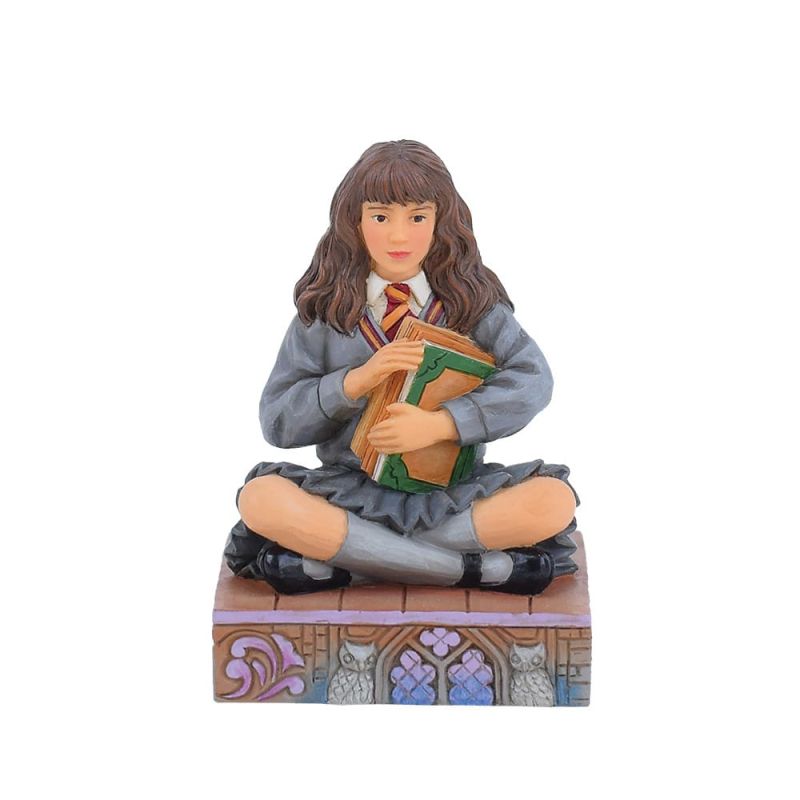 Een beeldje van Hermione Granger, die boeken vasthoudt en op een stenen blok met uitgesneden details zit.