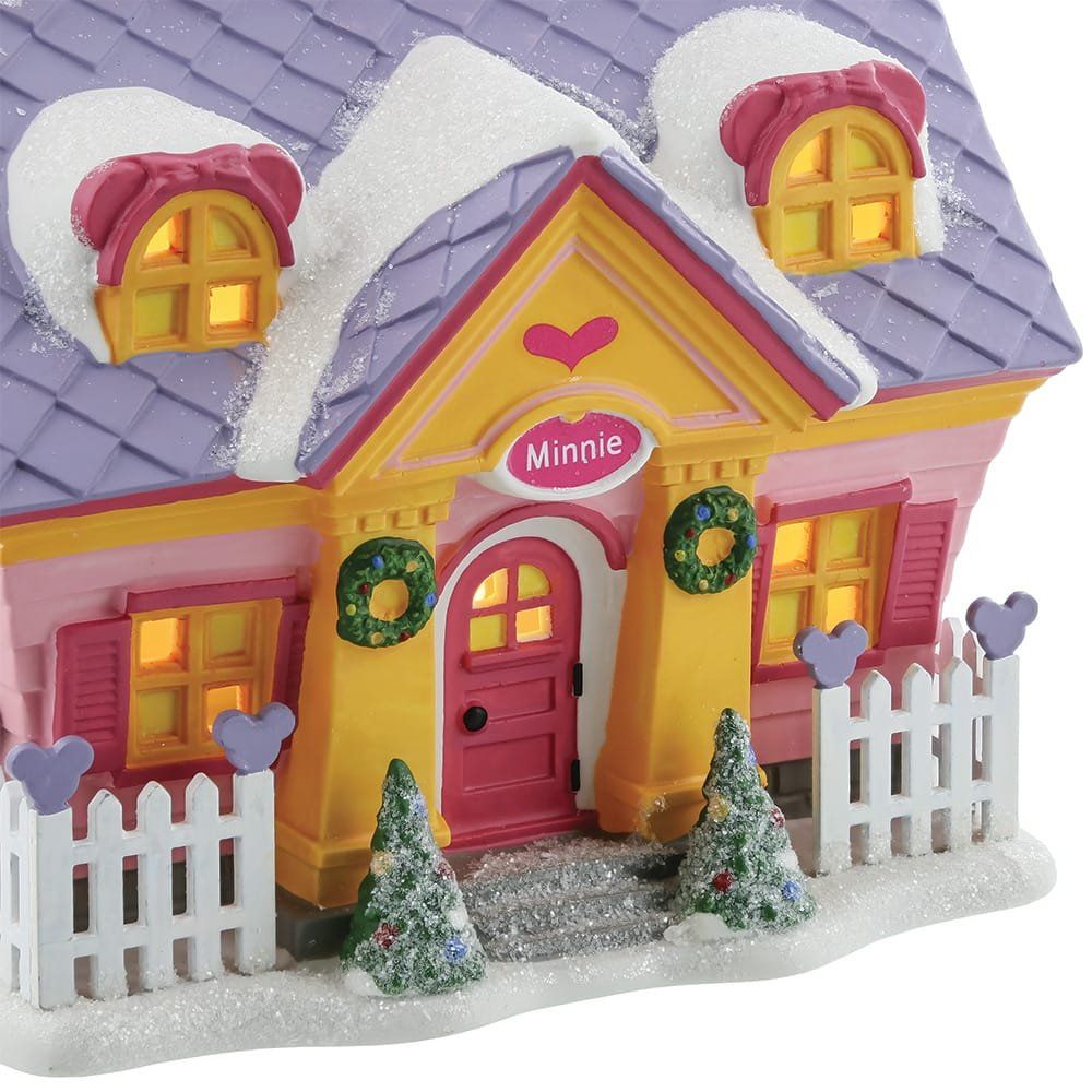 Kerstdorpje met huisje, roze en geel, paars dak bedekt met sneeuw, kransen en lichtjes.