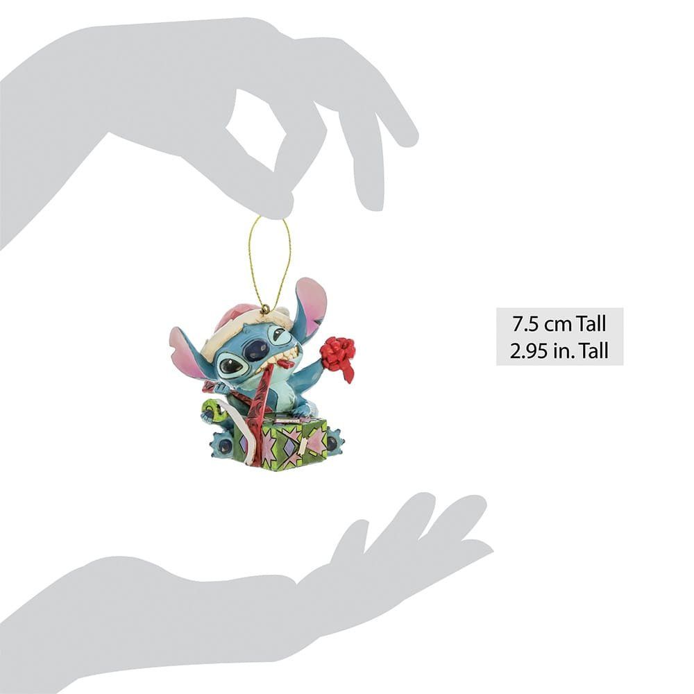 Kerstversiering van Stitch. Een blauw buitenaards figuurtje dat een rode bloem vasthoudt en op een geschenkdoos zit.