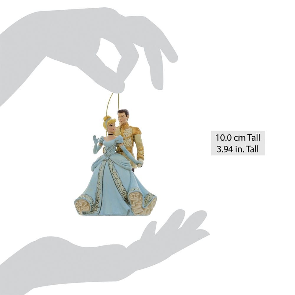 Ornament van Assepoester en Prins Charmant, in blauw en goud, vastgehouden door een hand.