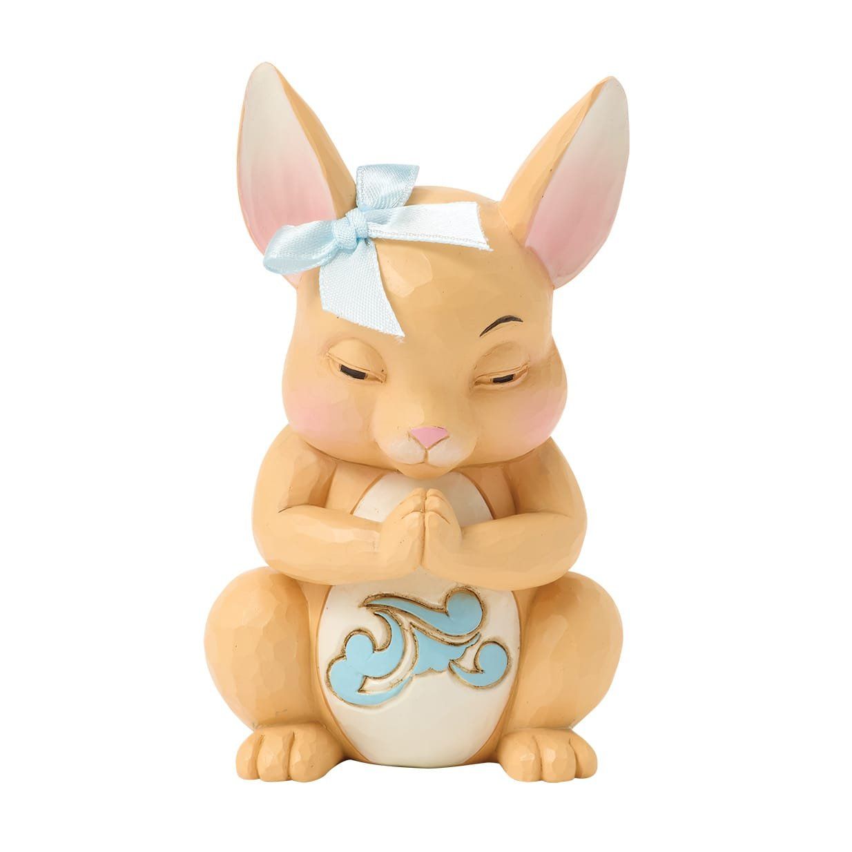 Een beige konijnenfiguurtje met een blauwe strik, de ogen gesloten in gebed en de handen ineengevouwen.