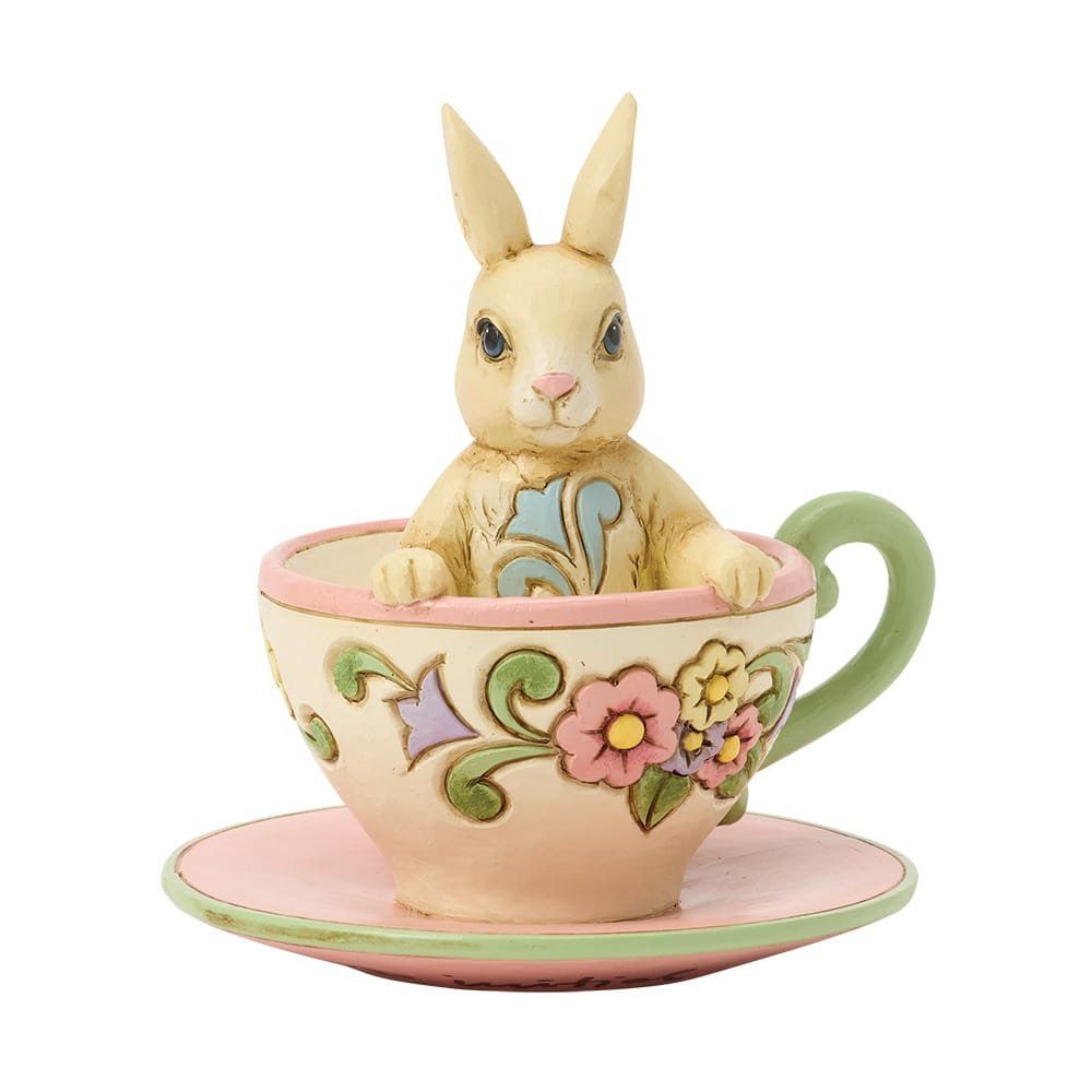 Crèmekleurig konijntje in een pastelkleurig theekopje met bloemmotief en een bijpassend schoteltje.