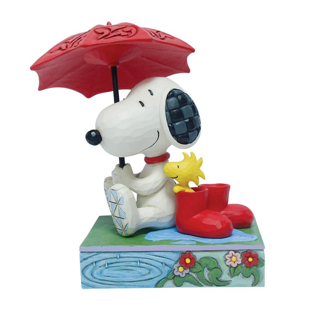 Snoopy en Woodstock staan onder een rode paraplu, naast rode laarzen op een doos met regendetails en bloemen.