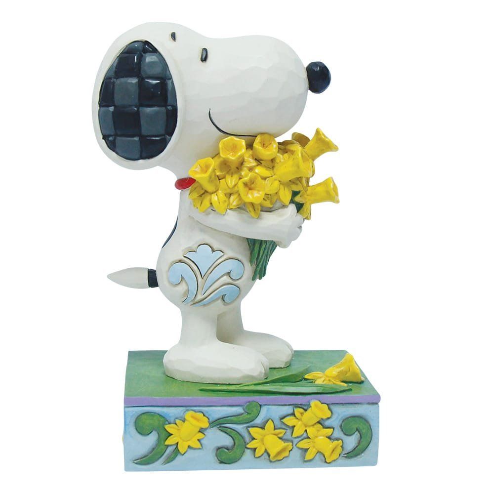 Een Snoopy-figuurtje met gele narcissen. Hij staat op een voetstuk versierd met bloemen.