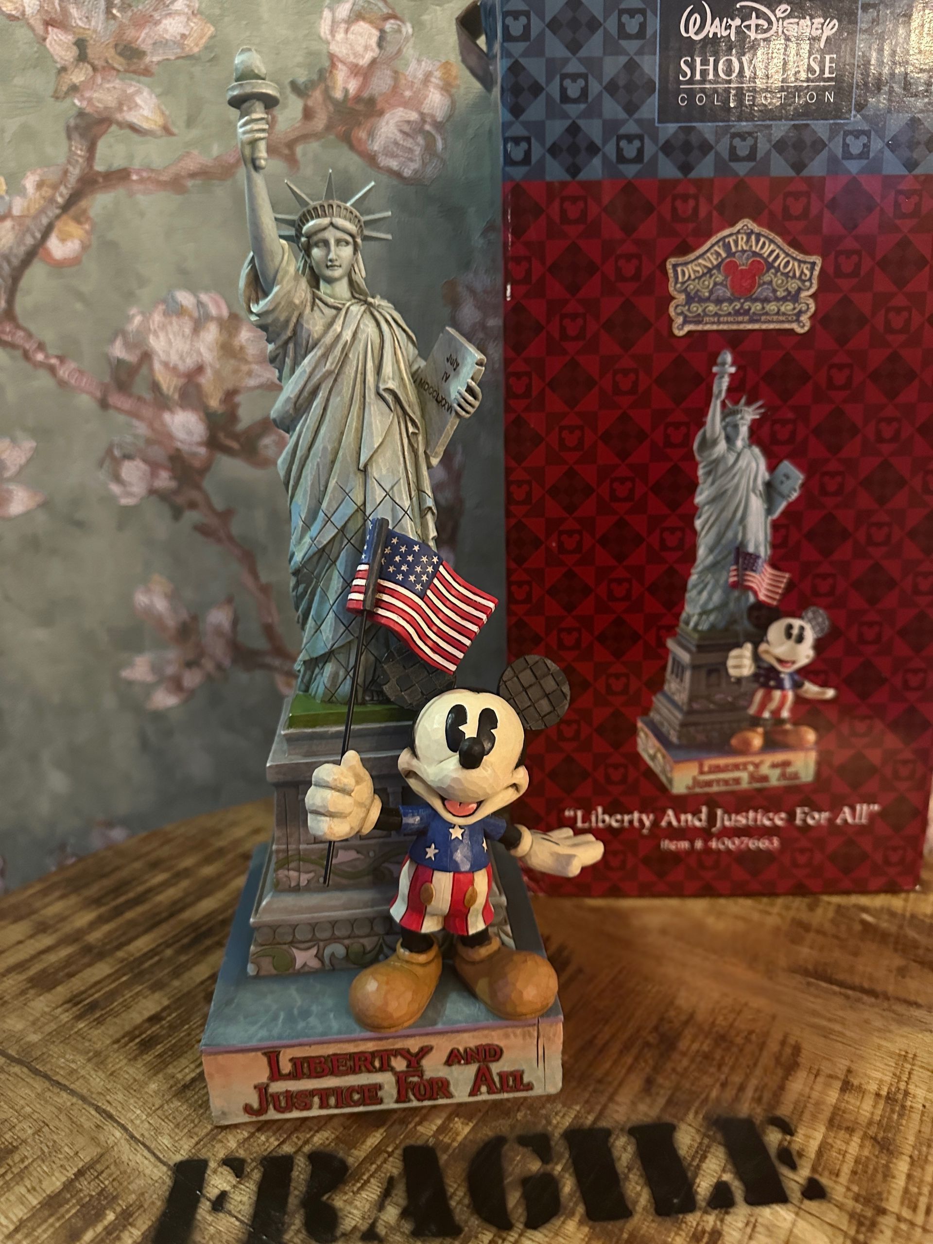 Een beeldje van het Vrijheidsbeeld met Mickey Mouse ervoor, een doos ernaast. Mickey draagt ​​patriottische kleding en houdt een vlag vast.