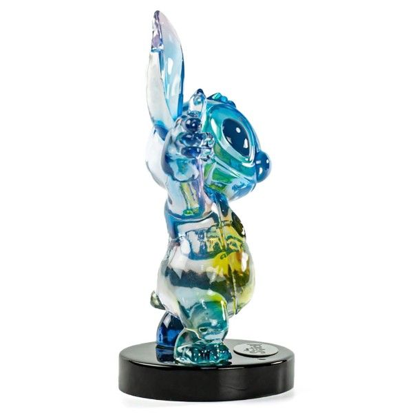 Blauwe, iriserende Stitch-figuur op een zwarte voet, met opgeheven arm en een expressief gezicht.