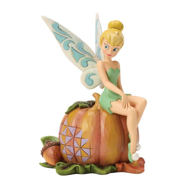 Tinkerbell zit bovenop een pompoen met herfstbladeren; ze heeft een lichtgroene jurk en blonde vleugels.