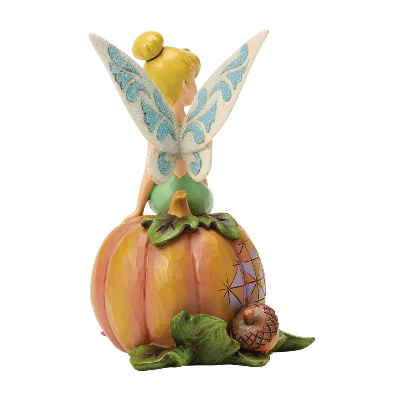 Een figuurtje van Tinkerbell zit op een pompoen met haar vleugels uitgespreid. De pompoen is oranje met groene bladeren.