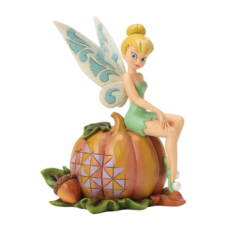 Tinkerbell zit bovenop een pompoen met herfstbladeren; ze heeft een lichtgroene jurk en blonde vleugels.