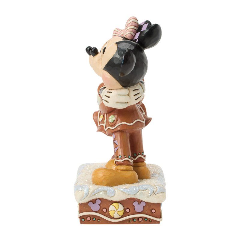 Een Minnie Mouse-figuurtje in peperkoekkostuum, staand op een versierde sokkel.