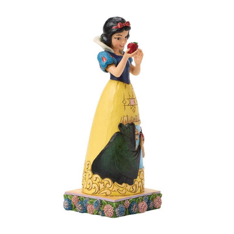 Sneeuwwitje-figuurtje met een rode appel in haar hand. Ze draagt een blauw, geel en zwart jurkje. Het figuurtje staat op een voetstuk met een bloemmotief.