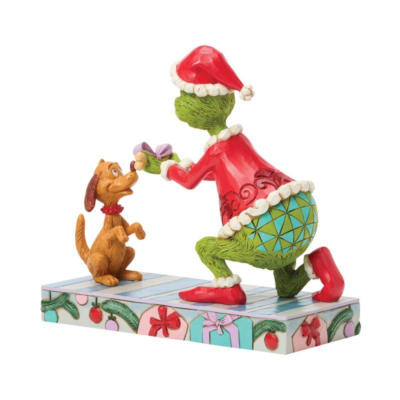 De Grinch in een rood pak knielt en geeft een cadeautje aan de hond Max. Kerstfiguurtje op een versierde sokkel.