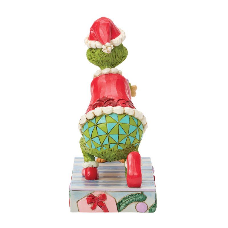 De Grinch biedt een cadeautje aan zijn hond Max aan, geplaatst op een versierde vensterbank. De Grinch is groen en draagt ​​een rood pak.